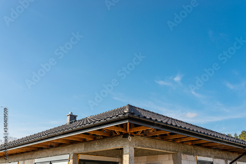 The roof of a single-family house covered with a new ceramic tile in anthracite against the blue sky, visible trusses.  © Michal