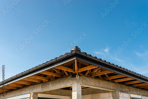 The roof of a single-family house covered with a new ceramic tile in anthracite against the blue sky, visible trusses. 