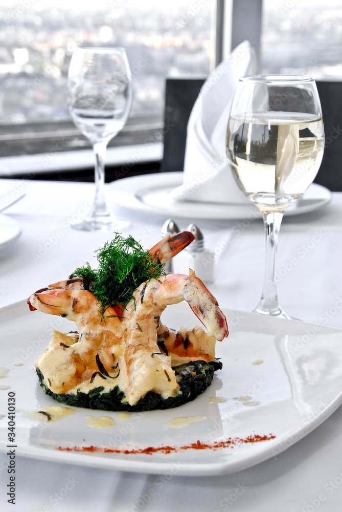 plato de camarones asados a la mantequilla con copa de vino blanco, sobre una mesa de restaurante, con vista panorámica a la ciudad y mantelería blanca  
