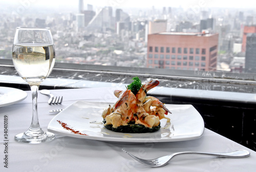 plato de camarones asados a la mantequilla con copa de vino blanco, sobre una mesa de restaurante, con vista panorámica a la ciudad y mantelería blanca   photo