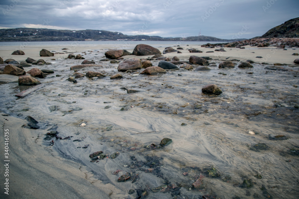 View of the sandy beach with stones at low tide in cloudy weather. Barents Sea village Teriberka. View of the sandy beach with stones at low tide in cloudy weather. Barents Sea village Teriberka.