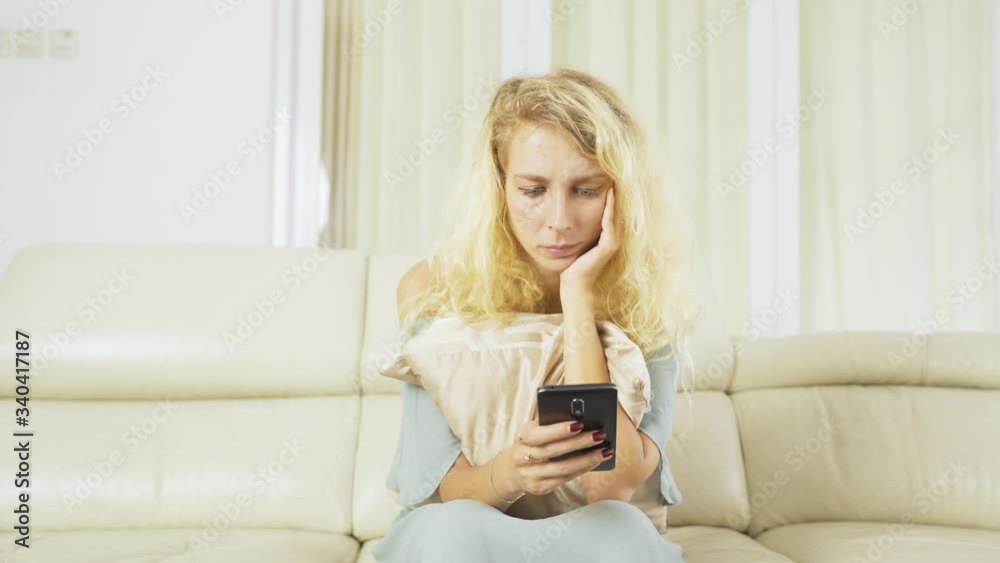 Young Caucasian woman looks bored while using a cellphone and sitting on the couch in the living room at home. Shot in 4k resolution Young Caucasian woman looks bored while using a cellphone and sitting on the couch in the living room at home. Shot in 4k resolution
