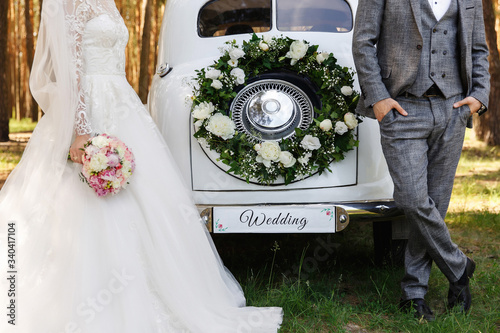 Stylish wedding couple, elegant newlyweds, groom and bride posing near white Just Married car with inscription ''Wedding''