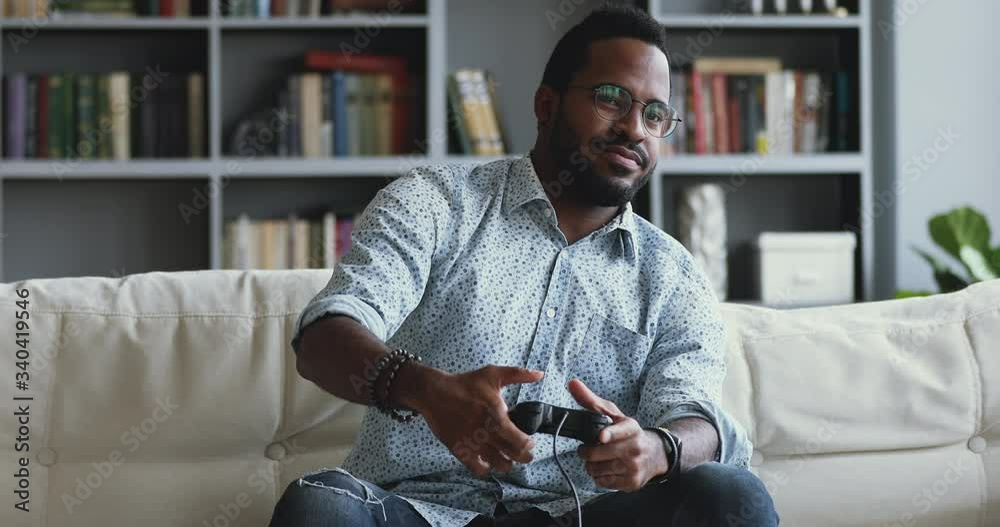 Addicted to technology young african american hipster man holding joystick, playing online console car racing shooting videogame alone at home, feeling dissatisfied with losing round, hobby concept.