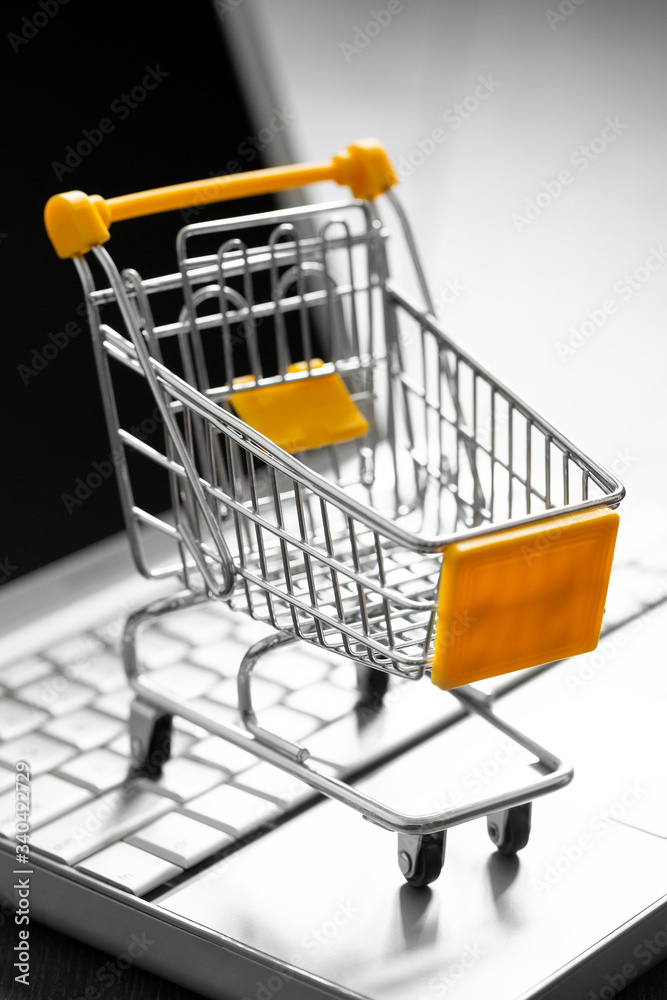Small yellow shopping cart on laptop. Technology business online shopping concept
