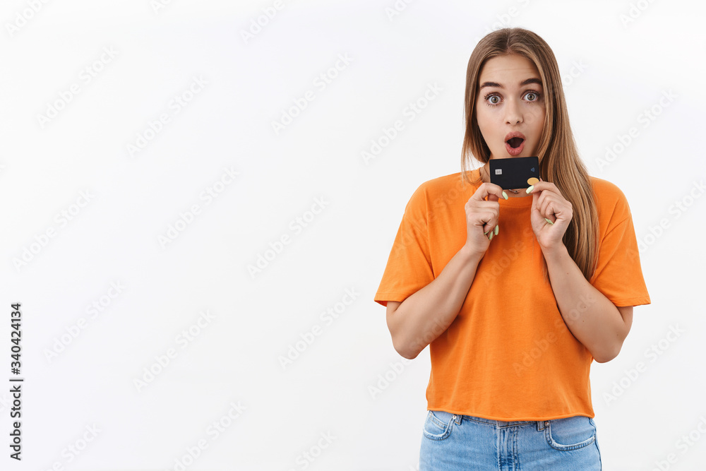 Portrait of surprised, excited blond girl in orange t-shirt cant wait to waste all her money on new dress for summer vacation, holding credit card, staring camera impressed, shopping online Portrait of surprised, excited blond girl in orange t-shirt cant wait to waste all her money on new dress for summer vacation, holding credit card, staring camera impressed, shopping online