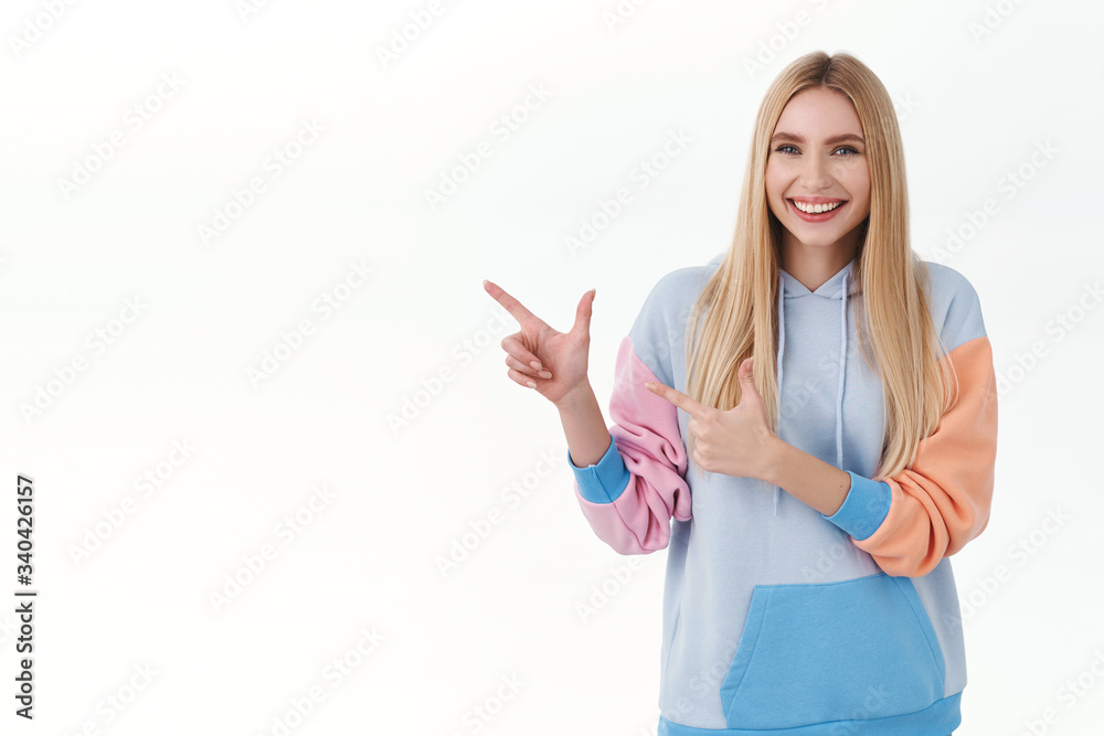 Portrait of caucasian cheerful blond girl in hoodie, pointing fingers left, presenting promo offer, give advice where find products, shopping site, smiling camera rejoice, recommend advertisement Portrait of caucasian cheerful blond girl in hoodie, pointing fingers left, presenting promo offer, give advice where find products, shopping site, smiling camera rejoice, recommend advertisement