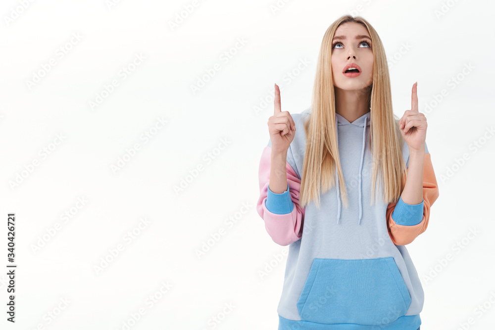 Curious blond attractive girl look intrigued up, raise head and pointing fingers at top promo, seeing something unique and unfamiliar, studying chart, reading banner, standing white background Curious blond attractive girl look intrigued up, raise head and pointing fingers at top promo, seeing something unique and unfamiliar, studying chart, reading banner, standing white background