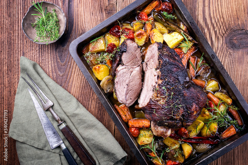Traditional barbecue lamb roast sliced with tomatoes and fried potatoes as top view in a metal tray