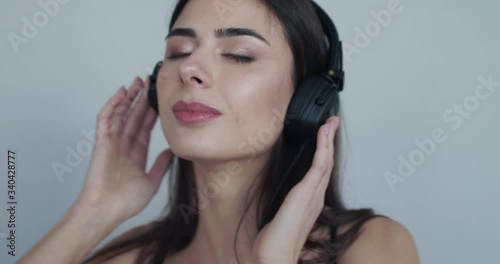 Girl listening to music on headphones with closed eyes and rejoices at camera