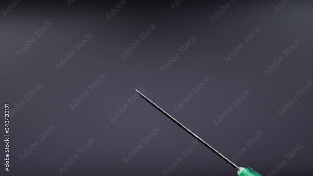 A syringe needle releases a drop of clear liquid A syringe needle releases a drop of clear liquid