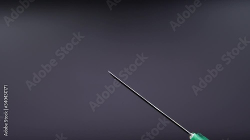 A syringe needle releases a drop of clear liquid