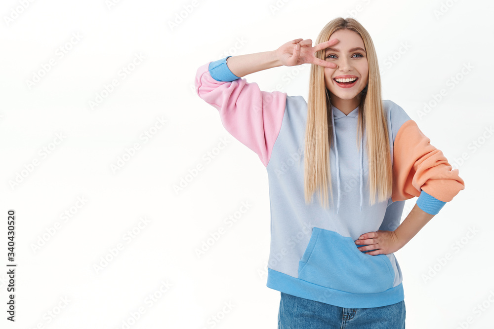 Attractive, enthusiastic caucasian blonde girl in stylish hoodie, showing peace sign over eye and smiling happy, express excitement and joy, feel happy, enjoying summertime, white background Attractive, enthusiastic caucasian blonde girl in stylish hoodie, showing peace sign over eye and smiling happy, express excitement and joy, feel happy, enjoying summertime, white background