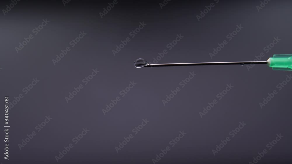 A syringe needle releases a drop of clear liquid A syringe needle releases a drop of clear liquid