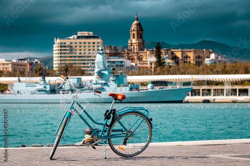 Aqua blue bicycle stands on the harbor, in background The Cathedral of Malaga