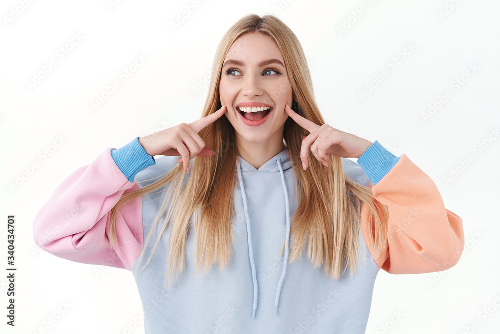 Naklejka premium Beauty, lifestyle and fashion concept. Upbeat good-looking blond girl poking her cheeks and smiling, looking away with joyful, happy emotion, promote skincare cosmetics or makeup