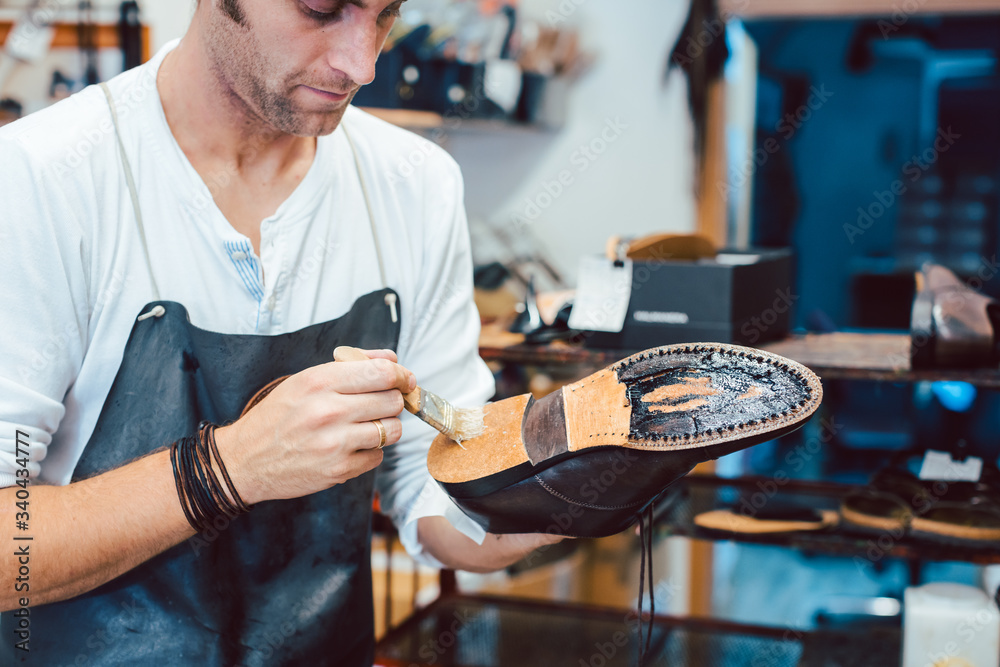 Obraz premium Shoemaker putting glue on sole of a shoe