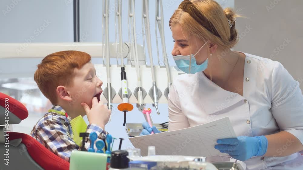 Female dentist writes on a medical card the symptoms of a boy patient. Pediatric dentistry