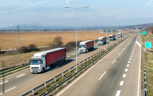 Convoy of transportation  trucks in line as a caravan or convoy on a country highway under an amazing blue sky © Ivan