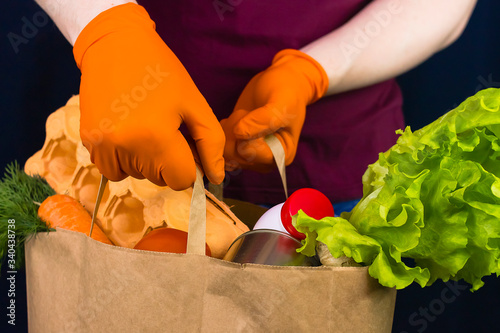Fotografi Delivery man wearing protective gloves holds paper bag with food