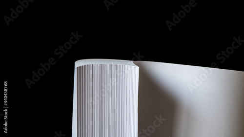 Studio photo of multiple sheets of rolled A4 paper stack (S-shaped ream) on black background. Simple, isolated object with copy space perfect for illustrating various concepts. Selective focus (shallo