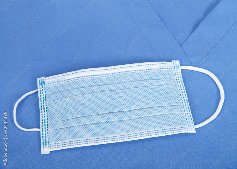 Top view flat lay of one surgical mask laying on blue scrub top.