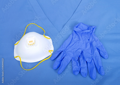 Top view flat lay of one N95 medical grade mask with blue latex gloves laying on scrub top uniform © sheilaf2002