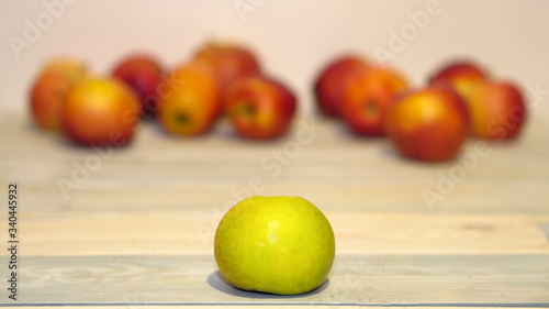 Green Apple close up on a white wooden table against a background of red apples