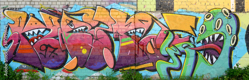 Abstract colorful fragment of graffiti paintings on old brick wall with scary octopus face. Street art composition with parts of unwritten letters and cartoon character photo