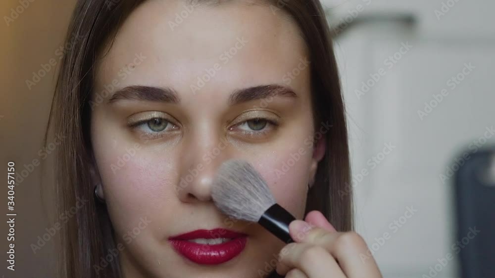 Portrait shot of the young pretty female beauty video blogger teaching how to do makeup and doing her forehead and cheeks with powder in front of the camera. Portrait shot of the young pretty female beauty video blogger teaching how to do makeup and doing her forehead and cheeks with powder in front of the camera.