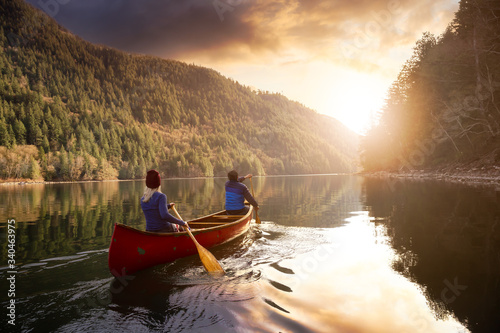 Fotografia, Obraz Couple friends canoeing on a wooden canoe during a colorful sunny sunset