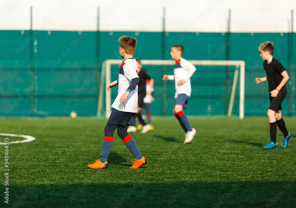 Boys in white black sportswear running on soccer field. Young footballers dribble and kick football ball in game. Training, active lifestyle, sport, children activity concept