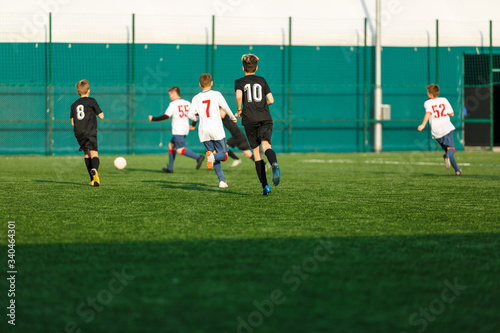 Boys in white black sportswear running on soccer field. Young footballers dribble and kick football ball in game. Training, active lifestyle, sport, children activity concept © Natali
