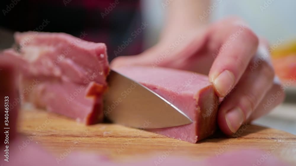 Young woman cuts the ham on a wooden cutting board, close-up Young woman cuts the ham on a wooden cutting board, close-up