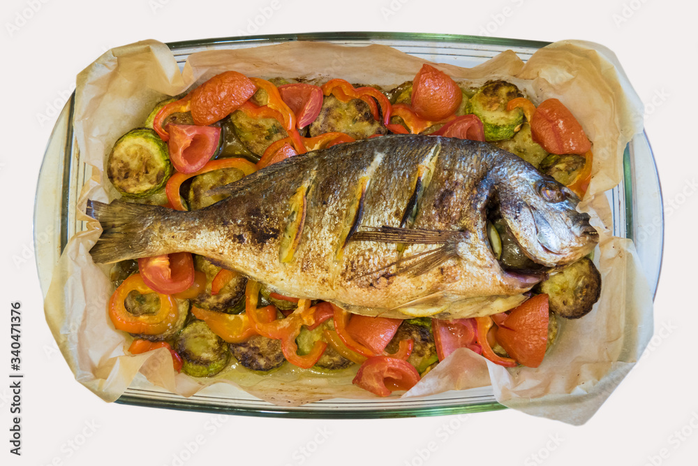 Top view on a glass dish with baked dorado fish with lemon and vegetables.
