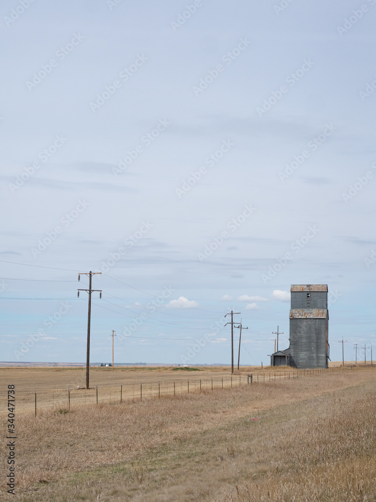 Old Metal Grain Elevator on the Prairie with power poles and field with dried grass in the foreground. Old Metal Grain Elevator on the Prairie with power poles and field with dried grass in the foreground.