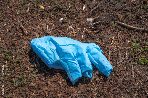 A used discarded blue latex glove lays discarded on some mulch in a parkway with fingers inside out during the COVID-19 coronavirus outbreak and pandemic.