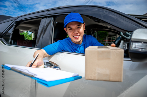 Asian delivery man in blue t-shirt on car send the box and document to sign. Delivery man concept.