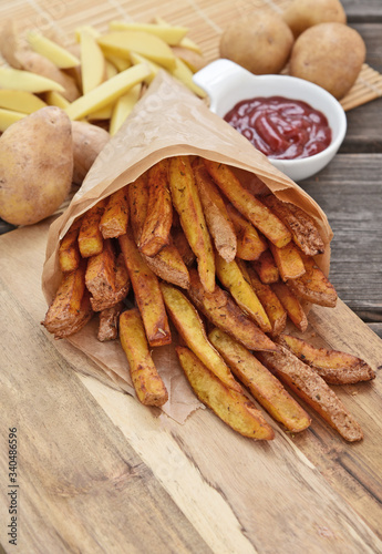 Homemade Crispy Seasoned French Fries..French fries  with spicy seasoning in brown paper bag on wooden broad.