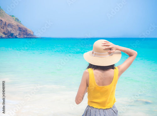 Woman with hat standing on blur image of on blue sea background. Summer and holiday concept.