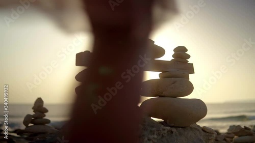 Young blonde girl laying a stone on a stone sculpture in a beach at dawn, close up, slow motion