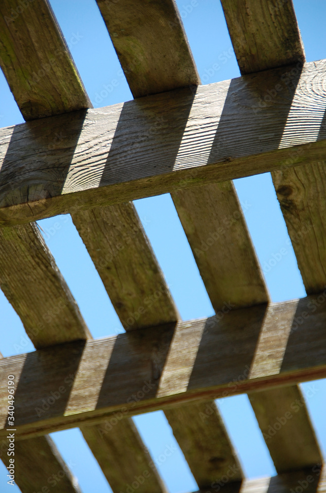 Wooden zig zag deck ceiling pattern with bright blue sky and long shadows in the afternoon light, wood texture and geometric patterns. Wooden zig zag deck ceiling pattern with bright blue sky and long shadows in the afternoon light, wood texture and geometric patterns.