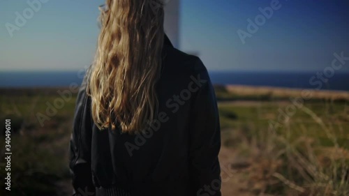 Young blonde photographer walks towards the lighthouse, close up to wide, slow motion