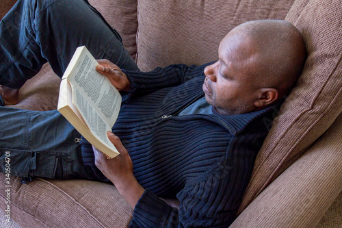 Black man, of African ethnicity, reading on the sofa
