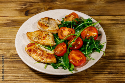 Fried chicken breast with salad of fresh arugula and cherry tomatoes on wooden table