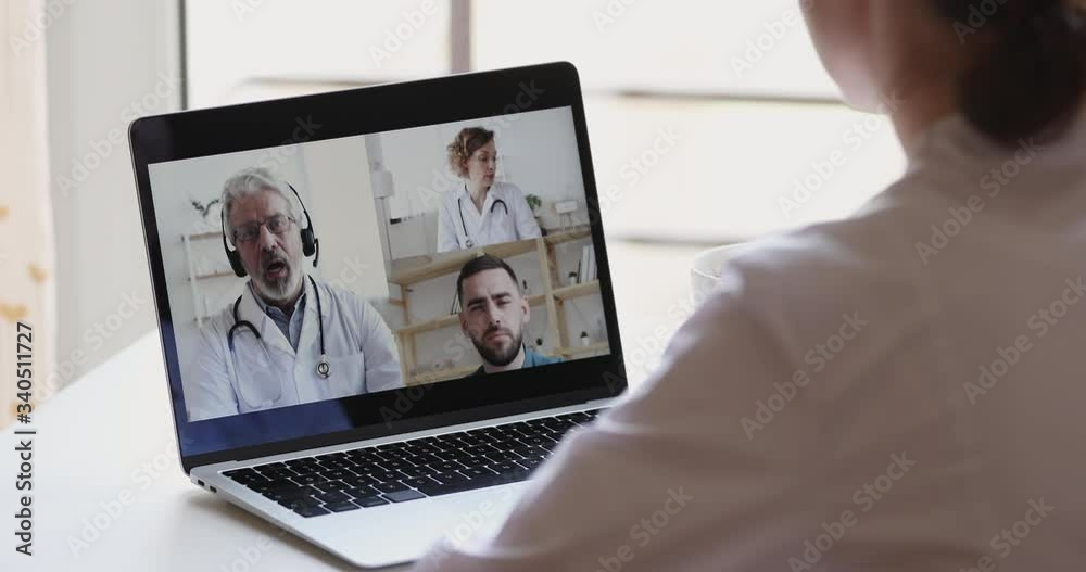 Female medical worker participate online webcam conference on laptop screen. Doctors group discuss healthcare during medic group video call virtual training webinar concept. Over shoulder closeup view