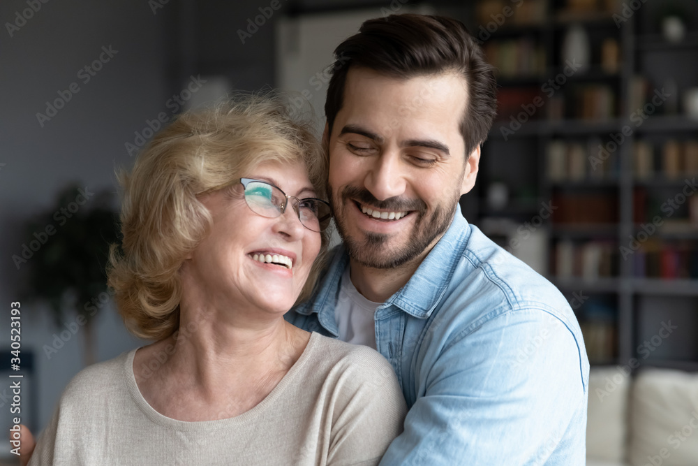 Close up middle-aged mother and her grown up millennial son embracing standing in living room at home, intergenerational family laughing enjoy time together. Care and love, best closest friend concept Close up middle-aged mother and her grown up millennial son embracing standing in living room at home, intergenerational family laughing enjoy time together. Care and love, best closest friend concept