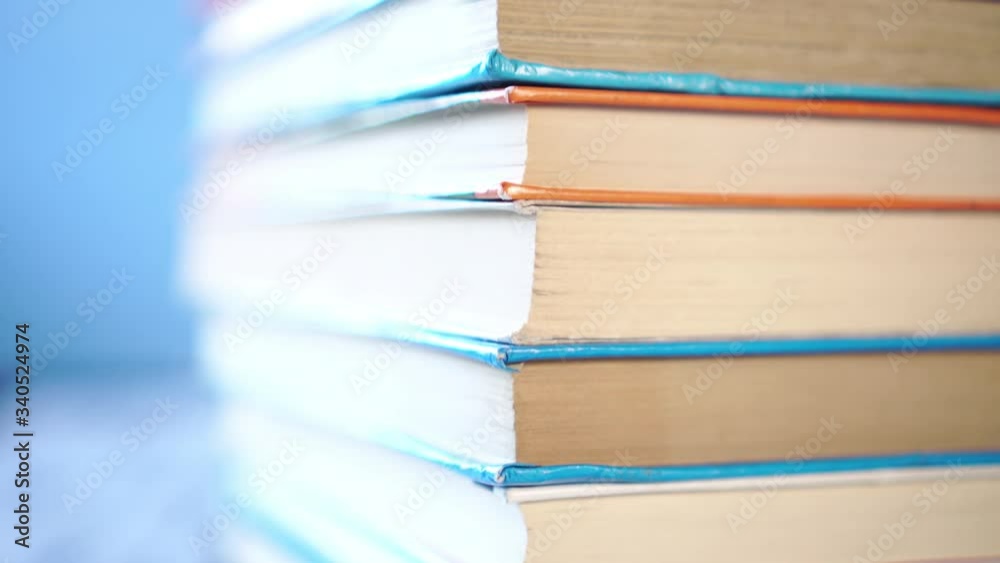 Corner of a stack of multi-colored books in hard and soft cover on a blue bright background. On a wooden old table. Close-up. Camera moves up
