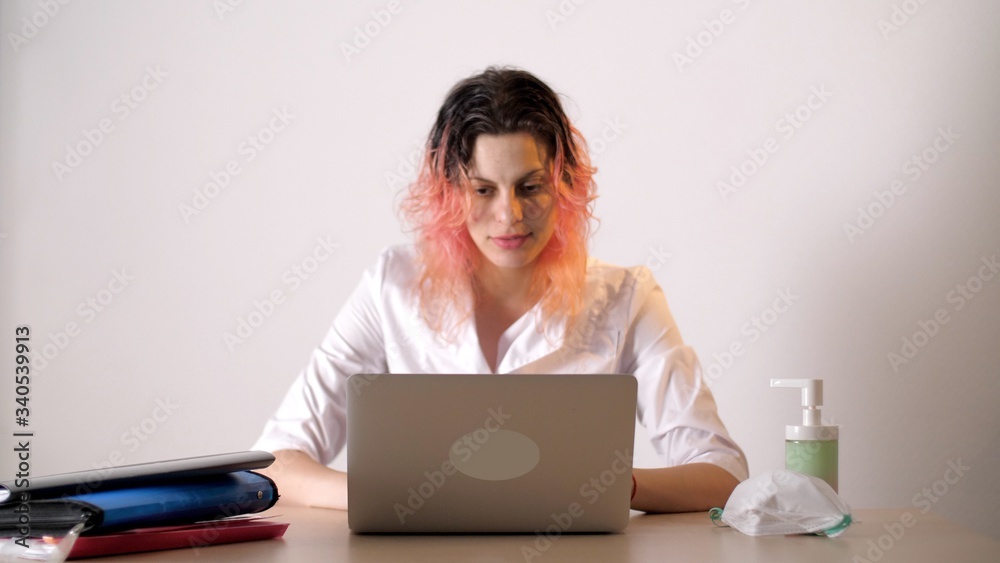 Female nurse in protective medical mask sitting at the table with laptop. Nearby is a liquid soap or sanitizer. Coronavirus or Covid-19. Female nurse in protective medical mask sitting at the table with laptop. Nearby is a liquid soap or sanitizer. Coronavirus or Covid-19.