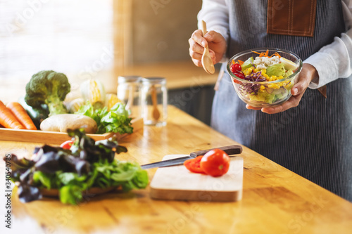 Closeup image of a female chef cooking and holding a bowl of fresh mixed vegetables salad to eat in kitchen
